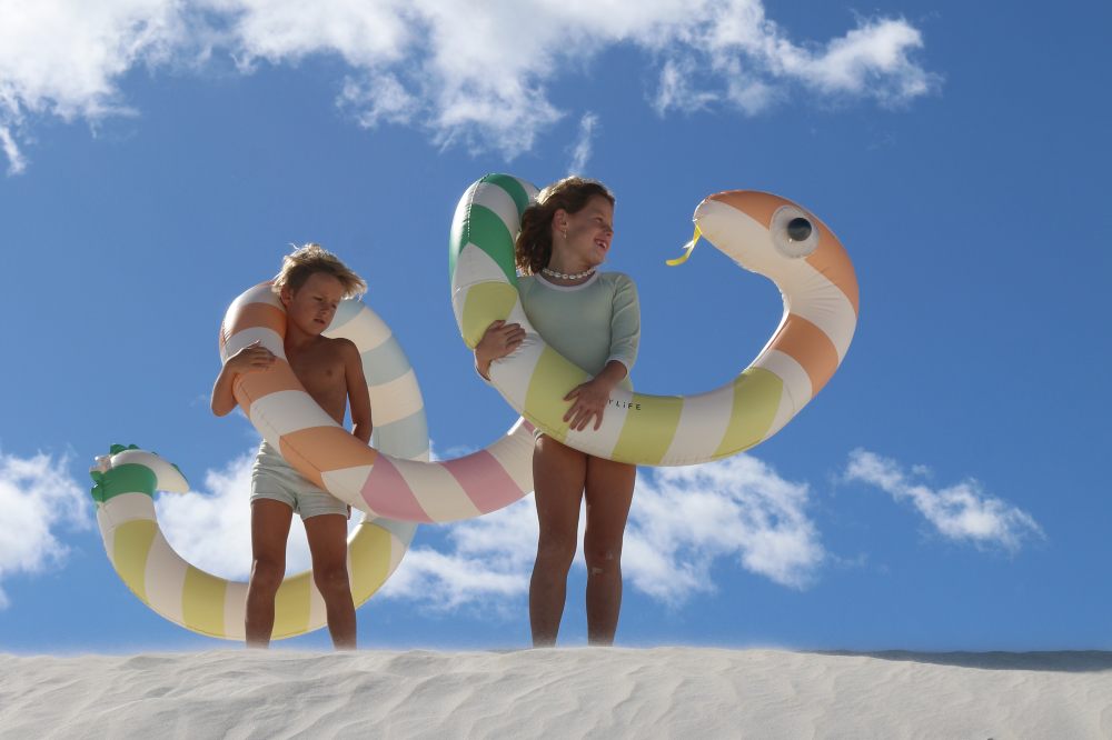 Two children stood on a sand dune holding a large inflatable snake by SUNNYLiFE