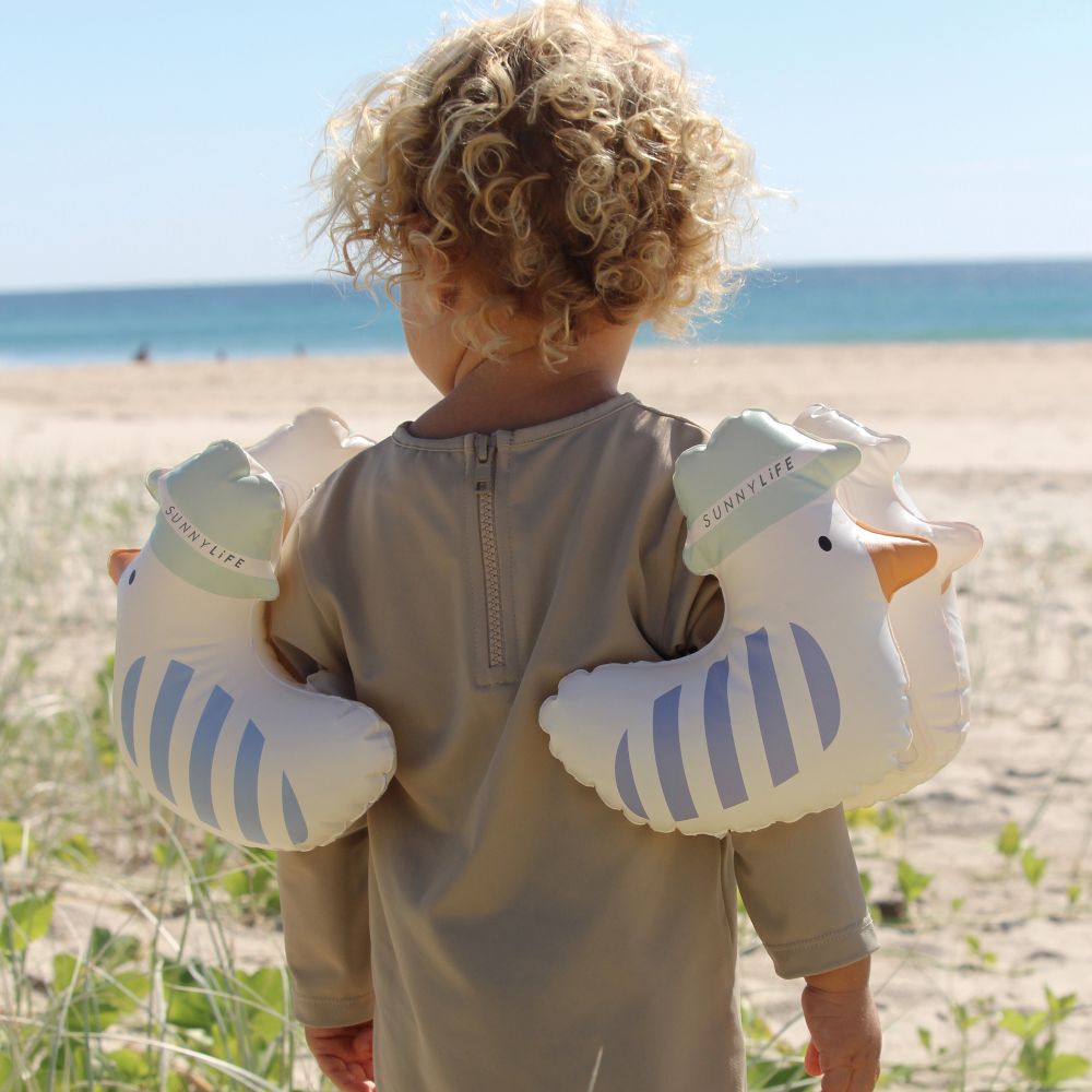 A child stood on a beach wearing duck armbands 