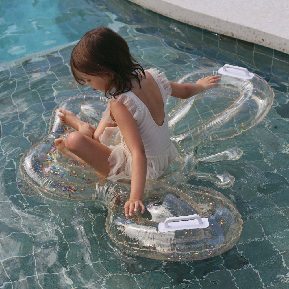 A young girl in a swimsuit floating on an clear butterfly inflatable in a pool 
