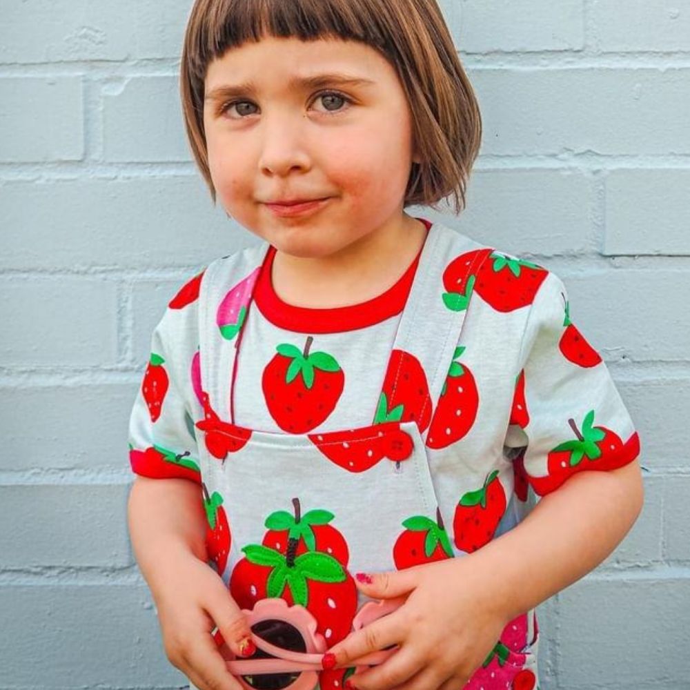 A young girl in a strawberry print T-shirt and dungarees 