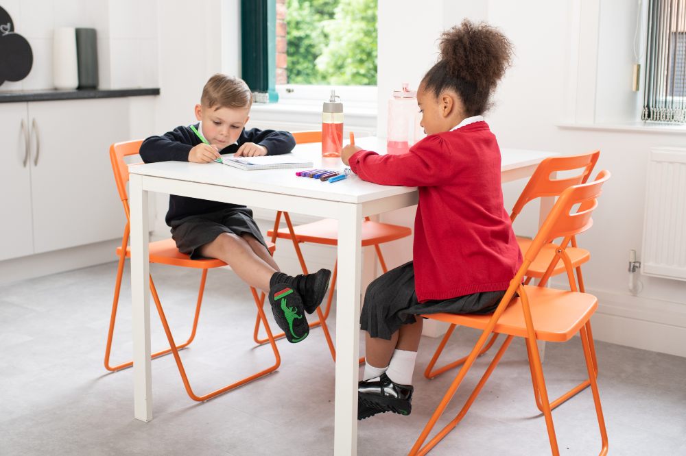 Two children sat a table wearing school uniform and school shoes by ToeZone