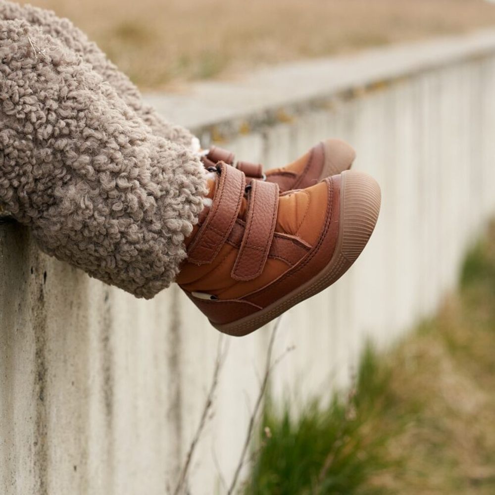 A pair of child's legs sat on a wall wearing fluffy trousers and brown leather shoes 
