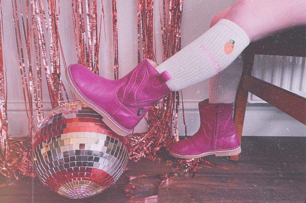 A child wearing pink boots resting their foot on a disco ball