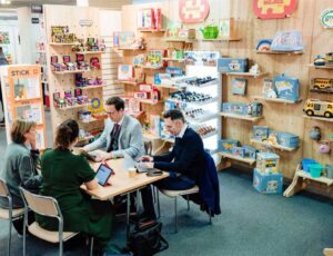 Two visitors sat down at a table with two exhibitors on a exhibition stand