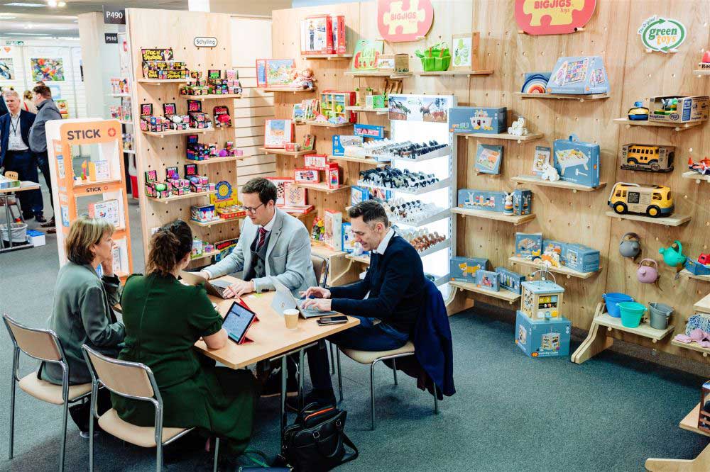 Two visitors sat down at a table with two exhibitors on a exhibition stand