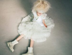 A girl sat on the floor wearing a white dress and white boots