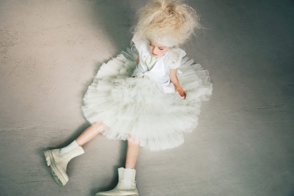 A girl sat on the floor wearing a white dress and white boots