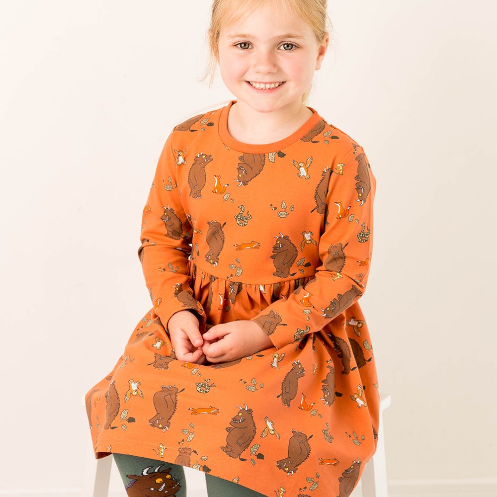 A young girl sat on a chair wearing an orange Gruffalo print dress 