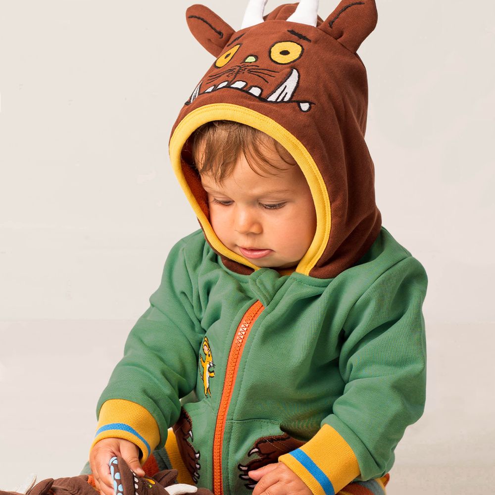 A young child sat on the floor looking downwards wearing a Gruffalo hooded jumper and leggings 