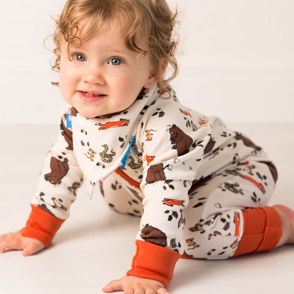 A young child crawling on the floor wearing a Gruffalo print babygro and matching bandana bib