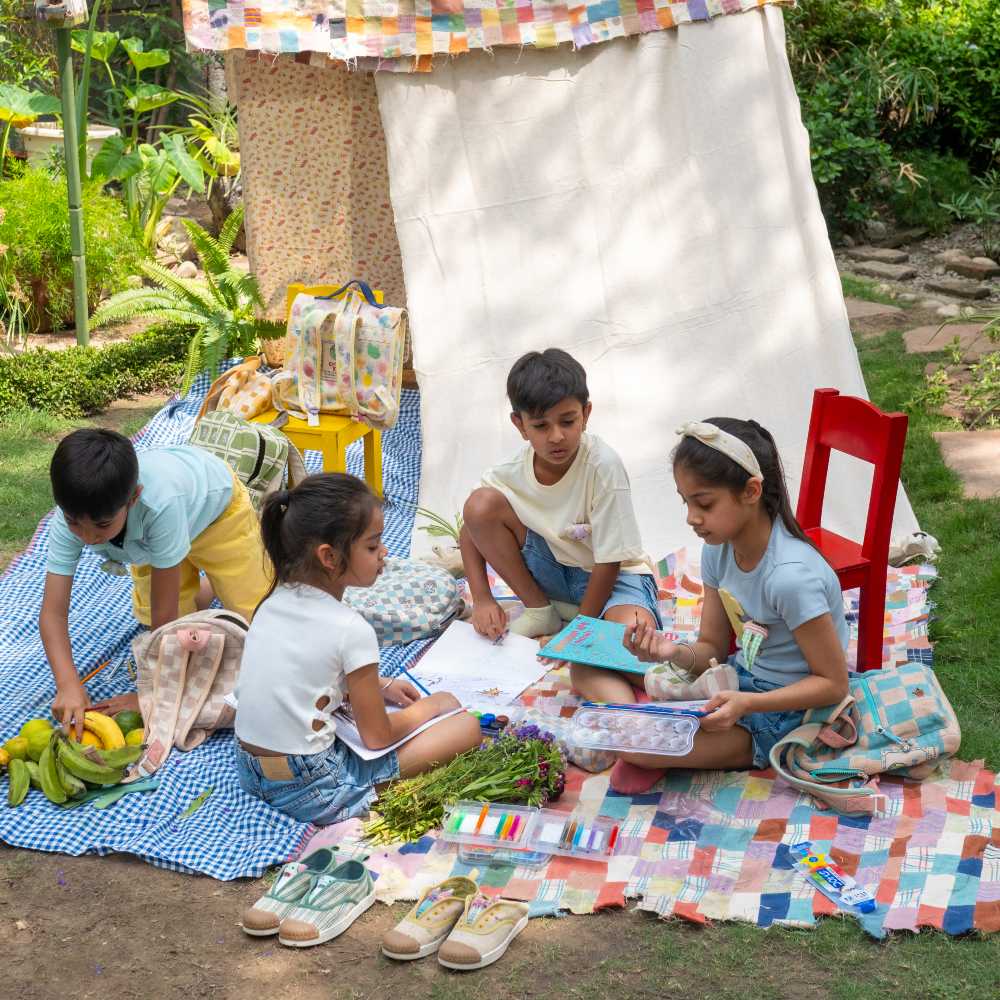 A group of children sat outside on fabric quilts 