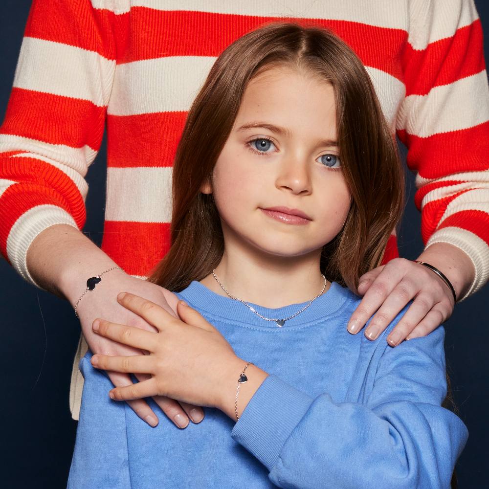 A young girl in a blue top reaching back to hold the hand of an adult stood behind