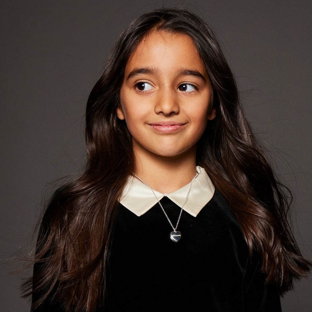 A young girl with long dark hair wearing a black dress with a white collar and a pendant necklace 