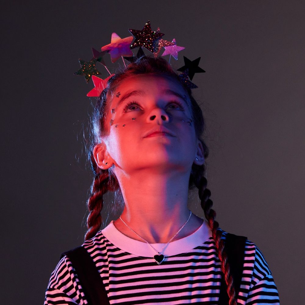 A young girl looking upwards wearing a star headdress and heart necklace by Little Star