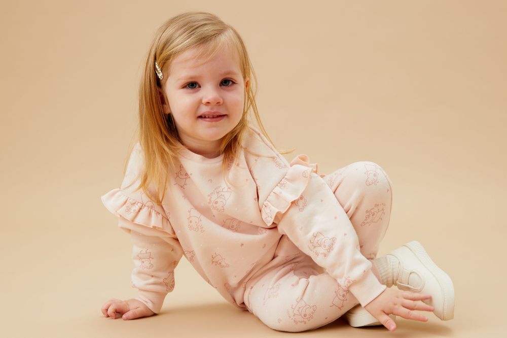 A young girl wearing a pink frilled top and trousers with Peppa Pig print on