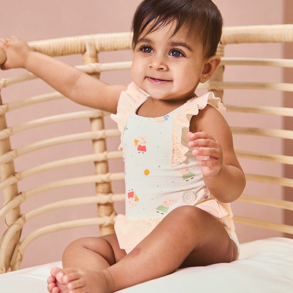 A baby sat in a chair wearing a swimsuit in a Peppa Pig print 