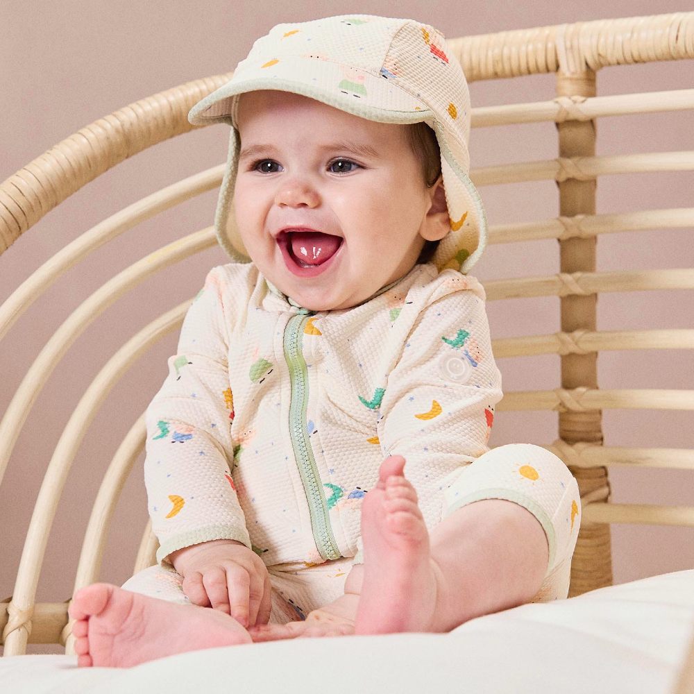 A young baby sat on a chair wearing a sunhat and sunsuit 