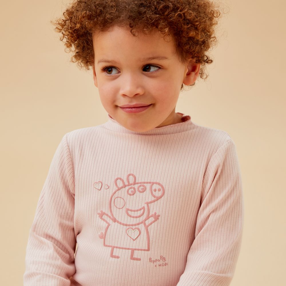 A young child wearing a pale pink top with a Peppa Pig motif on the front 