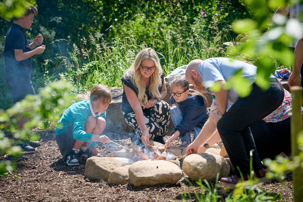 A group of school children and adults lighting a fire pit in the Nature School 