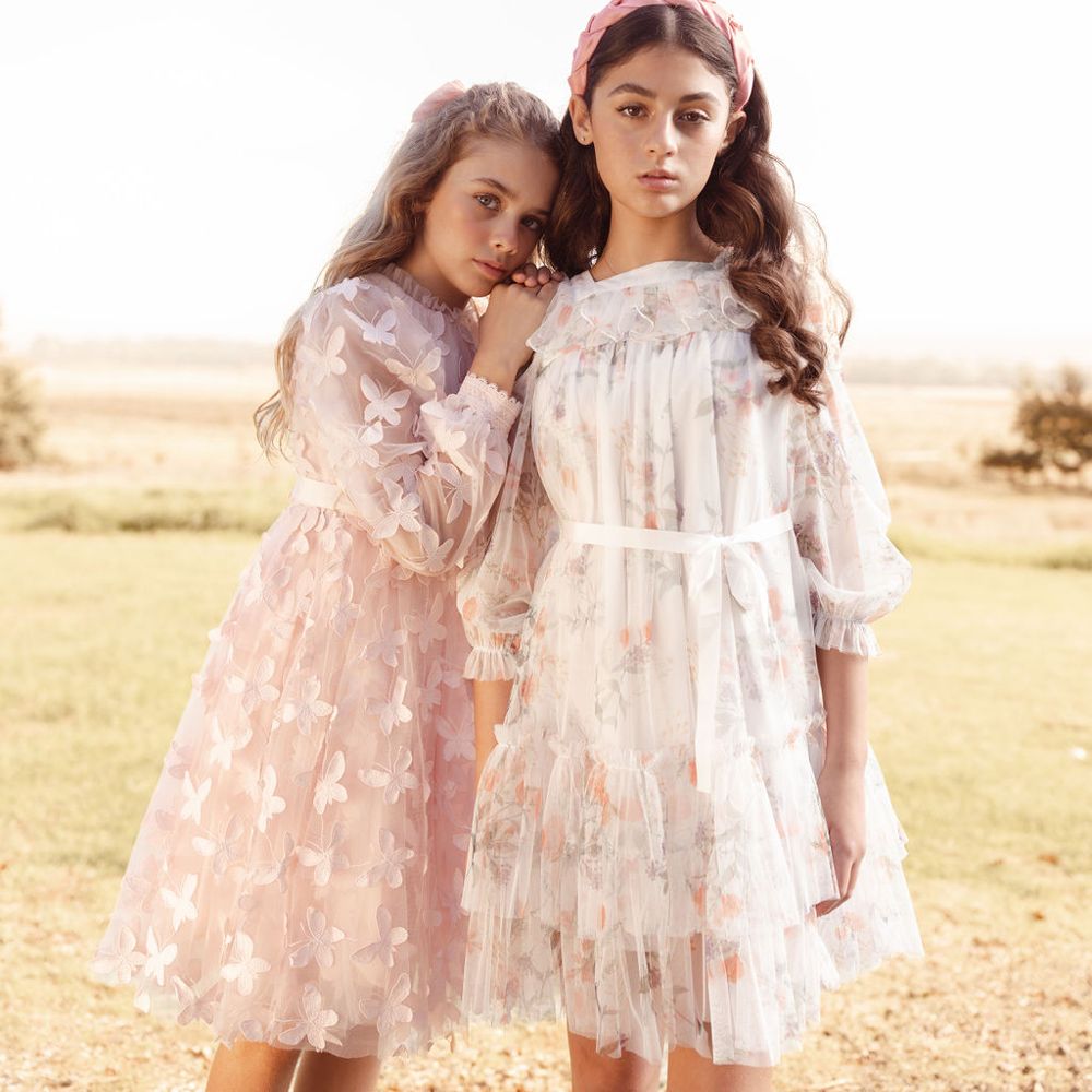 Two girls stood together in a field wearing occasionwear dresses