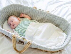 A young baby in a green and white striped top sleeping in a Moses basket