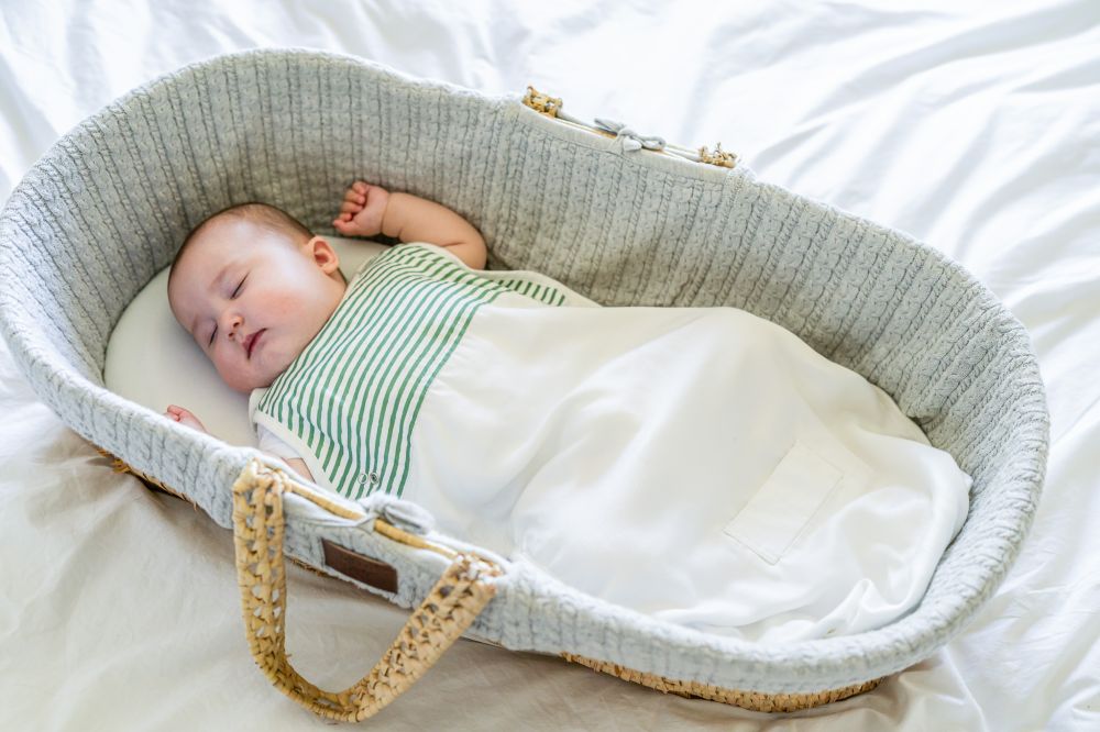 A young baby in a green and white striped top sleeping in a Moses basket