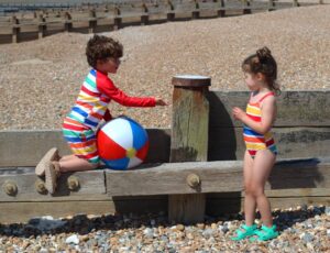 A young girl and boy on a beach wearing striped swimwear by Toby Tiger