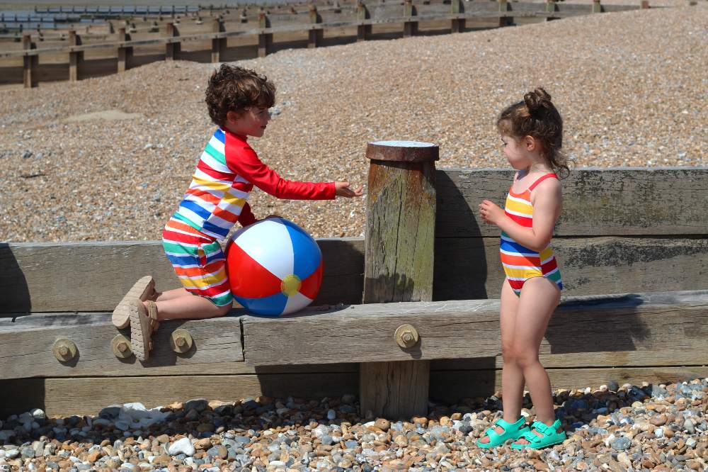 A young girl and boy on a beach wearing striped swimwear by Toby Tiger