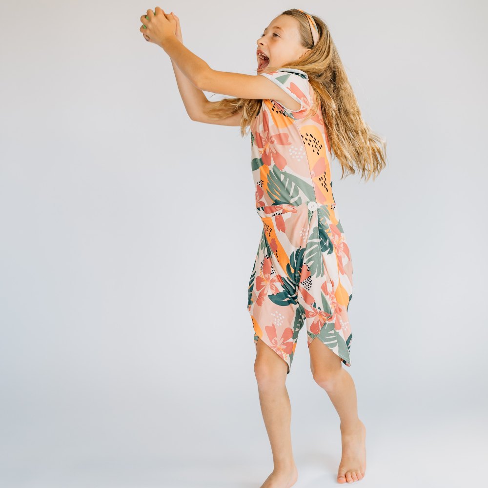 A girl wearing a patterned dress/romper holding her arms in the air 