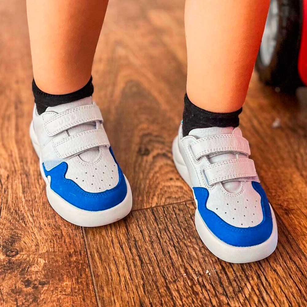 A young boy wearing a pair of blue and white Glide trainers