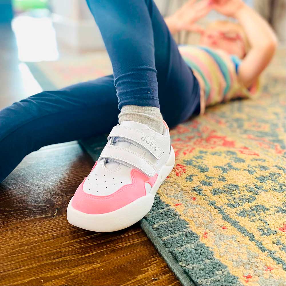 A young girl laid on the floor wearing a pair of pink and white Glide trainers