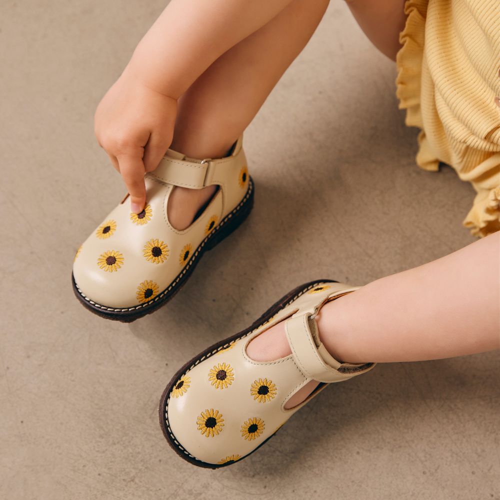 A close up of a child's feet wearing yellow shoes with sunflower motifs on