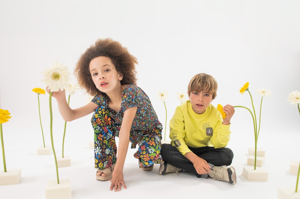 Two children knelt on the floor holding the stems of yellow flowers 