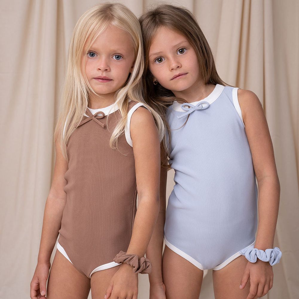 Two girls stood in front of a curtain wearing swimsuits by Bodi Loves 