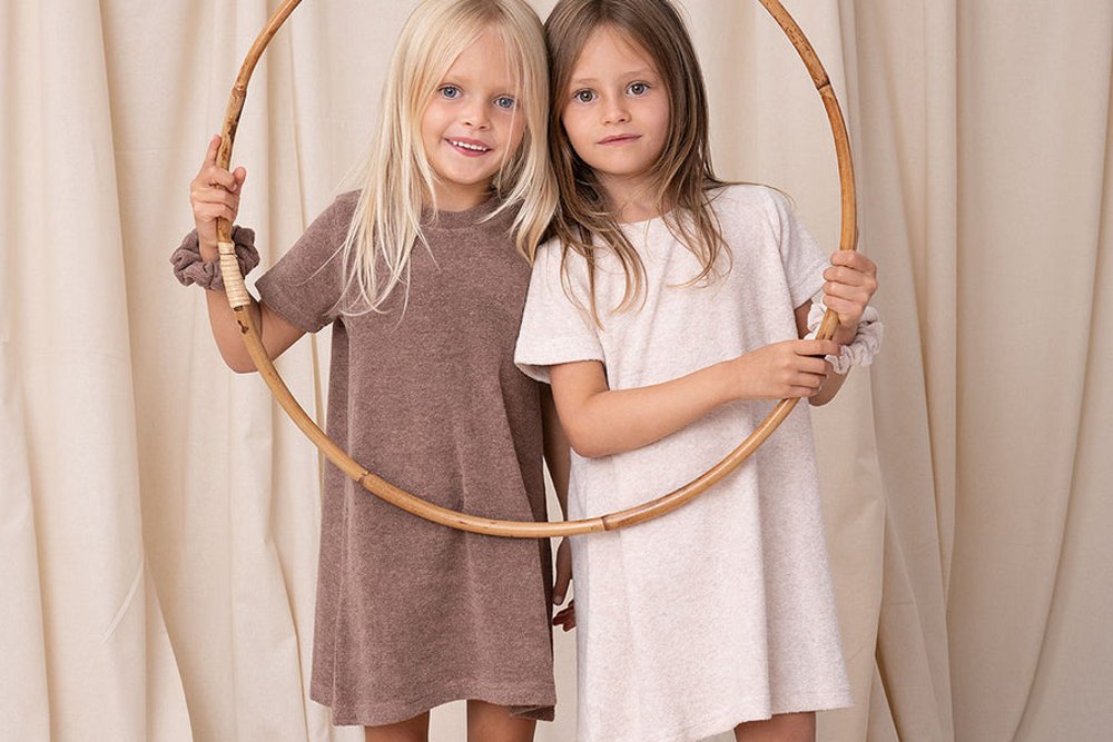 Two girls stood in front of a curtain holding a bamboo ring and wearing dresses by Bodi Loves