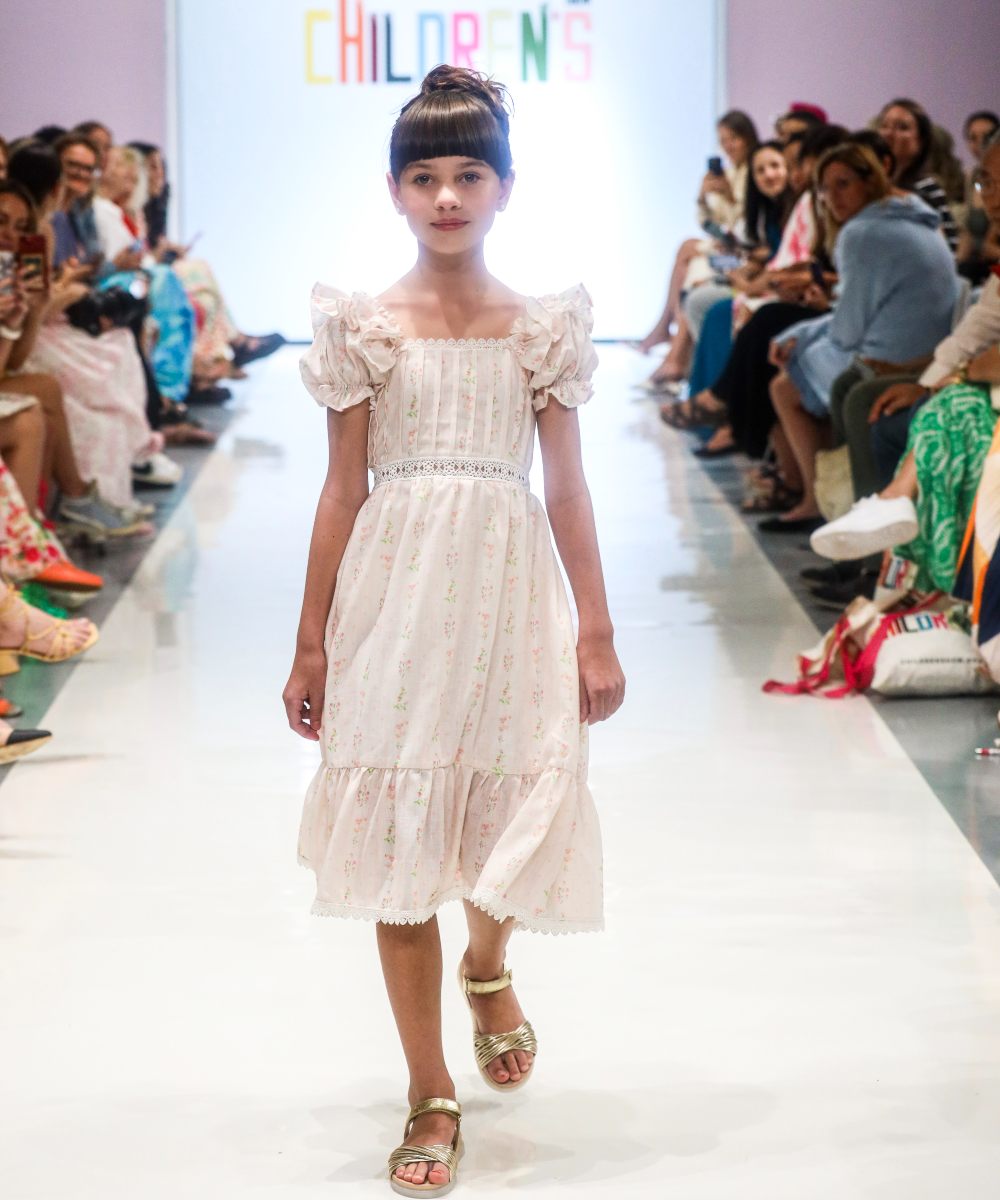 A girl on a fashion catwalk at Children's Show wearing a long white dress