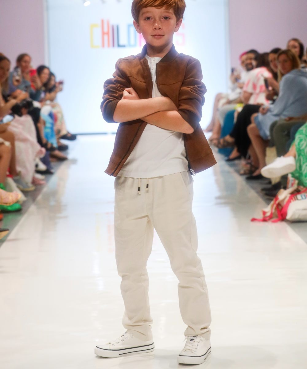 A boy on a fashion catwalk wearing a brown blazer and white top and trousers