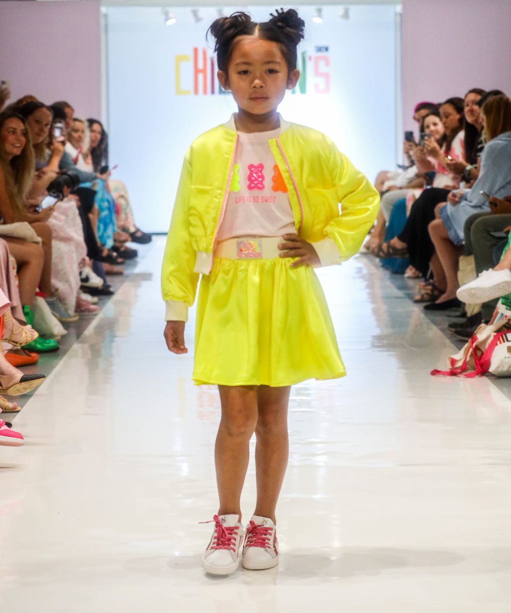 A girl on a fashion catwalk wearing a yellow jacket and skirt