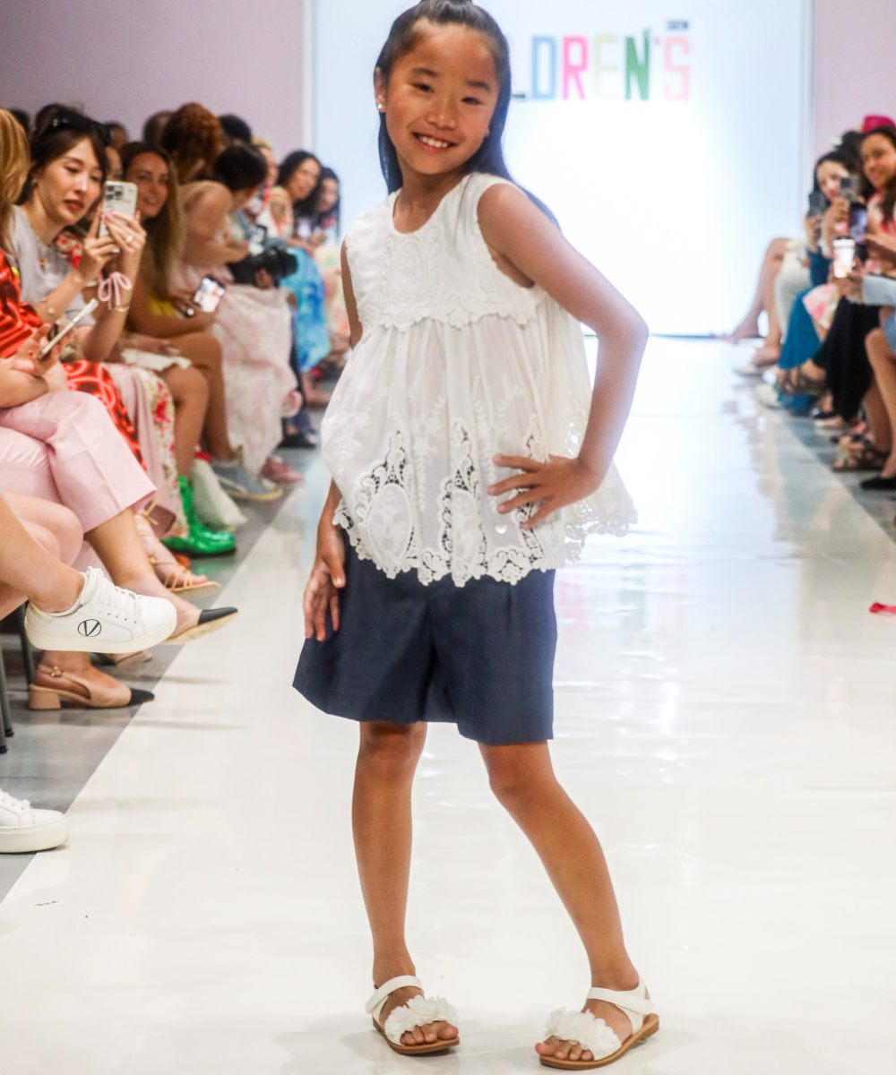 A girl on a fashion catwalk wearing a white top and navy skirt