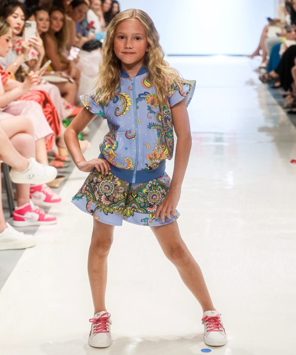 A girl in a patterned shirt and shorts on a fashion catwalk at Children's Show