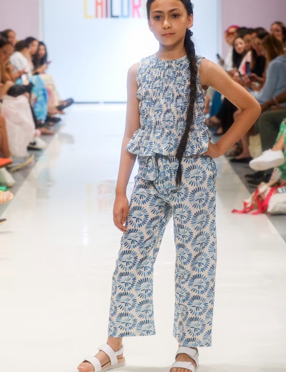 A young girl on a catwalk wearing a blue and white patterned top and matching trousers