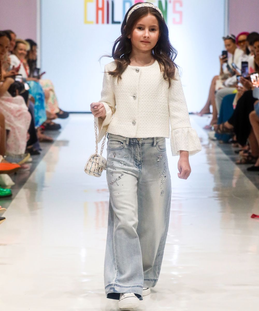 A young girl in headband, white shirt and jeans walking down a catwalk