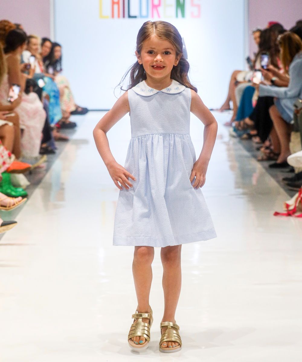 A girl in a blue collared dress walking on a catwalk