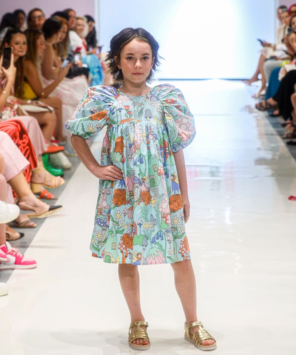 A girl on a catwalk in a floral print dress with short puff sleeves