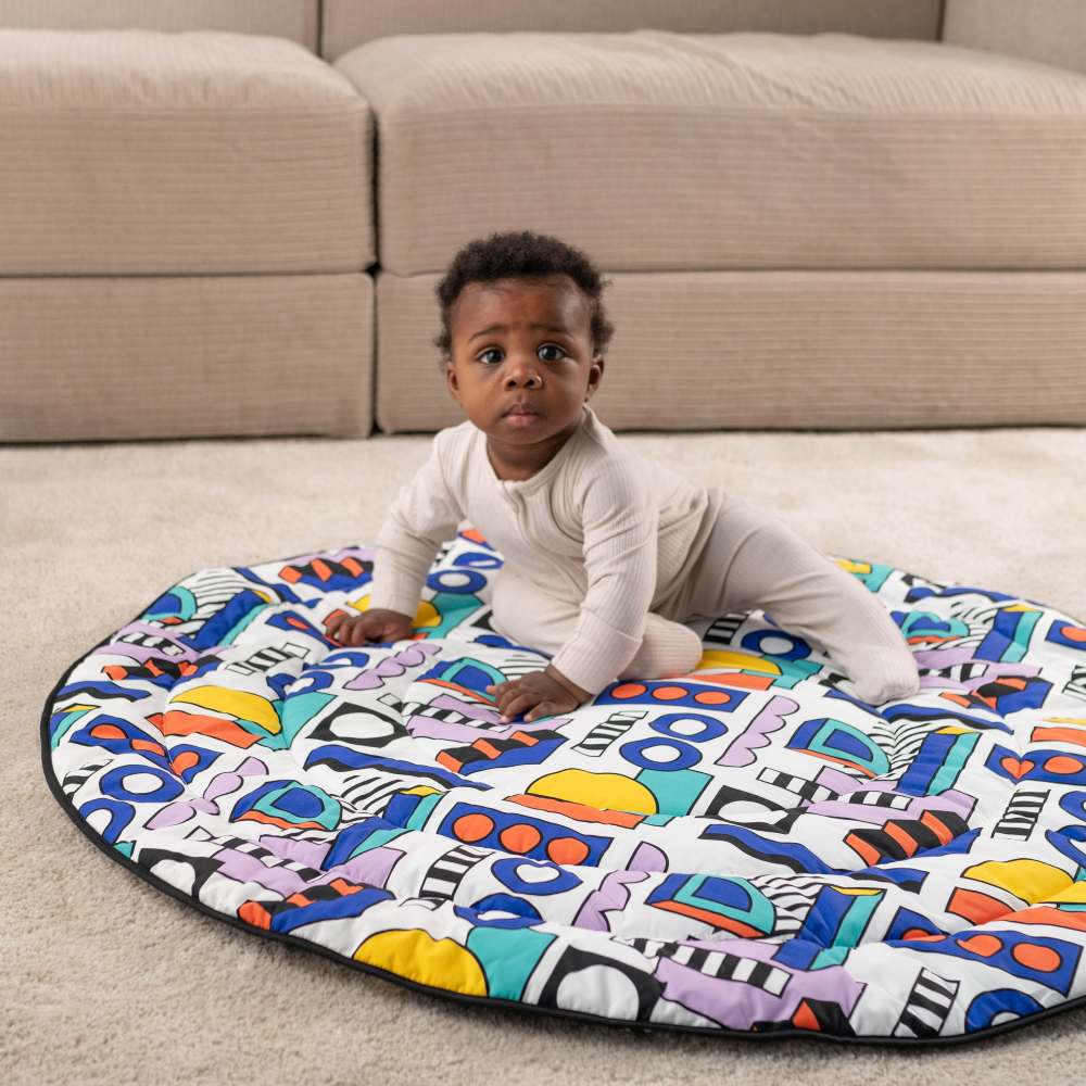 A young child sat on the floor on a brightly coloured playmat from the Etta Loves x Walala collaboration 