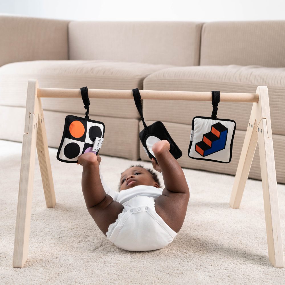 A baby lying on the floor playing with toys hanging from a wooden stand