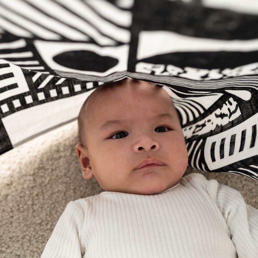 A young baby lying beneath a black and white print muslin from the Etta Loves x Walala collection 