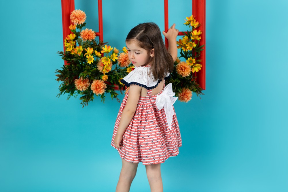 A young girl in a dress with a large bow on the back reaching up to a display of flowers 