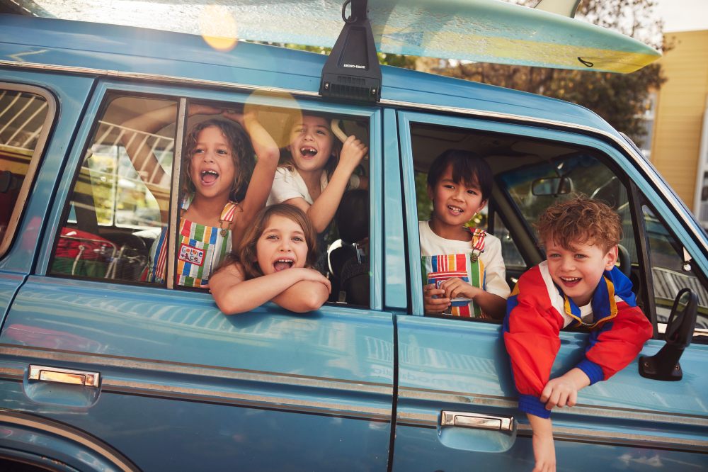 A group of children leaning out the windows of an old blue car 