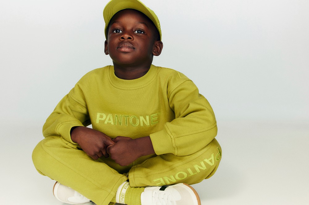 A young boy sat on the floor wearing a lime green cap, sweatshirt and joggers from the H&M x Pantone collection